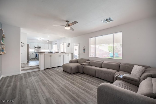 living room with ceiling fan, light wood-type flooring, visible vents, and baseboards