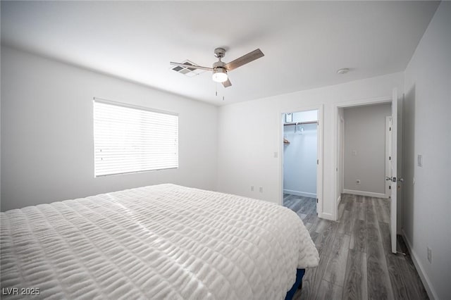 bedroom featuring a walk in closet, visible vents, ceiling fan, wood finished floors, and baseboards