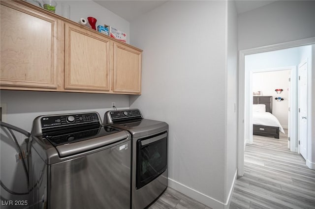 clothes washing area featuring light wood-style flooring, cabinet space, washer and clothes dryer, and baseboards