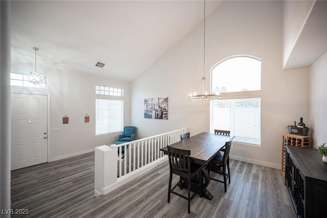 dining area featuring a notable chandelier, visible vents, wood finished floors, high vaulted ceiling, and baseboards