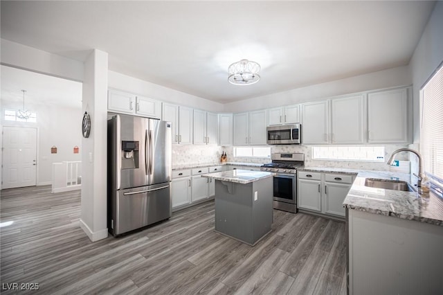 kitchen with an inviting chandelier, light stone counters, stainless steel appliances, and a sink