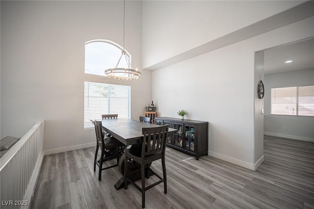 dining area featuring a chandelier, a towering ceiling, baseboards, and wood finished floors