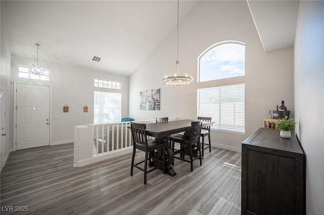 dining area featuring high vaulted ceiling, a notable chandelier, wood finished floors, visible vents, and baseboards