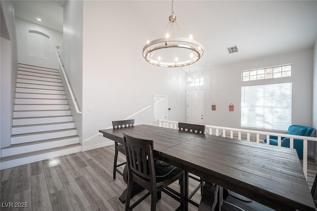 dining room featuring wood finished floors, visible vents, baseboards, stairs, and an inviting chandelier