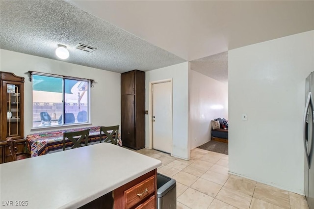 kitchen with light tile patterned floors, visible vents, light countertops, a textured ceiling, and stainless steel refrigerator with ice dispenser