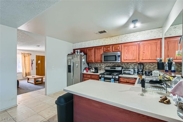 kitchen with a peninsula, backsplash, stainless steel appliances, and light countertops