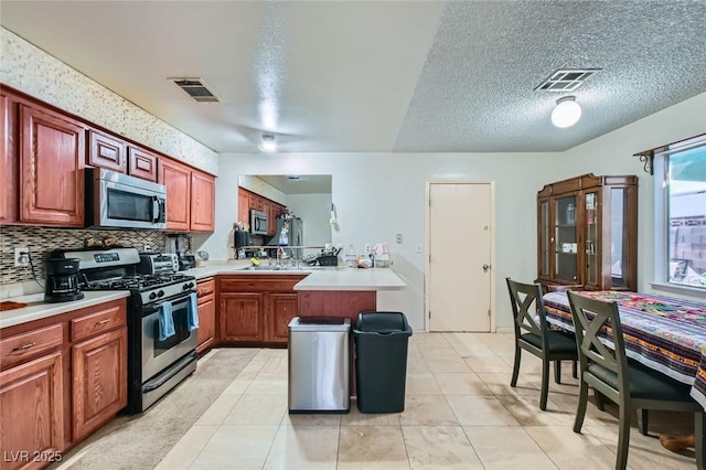 kitchen with appliances with stainless steel finishes, light countertops, visible vents, and a peninsula