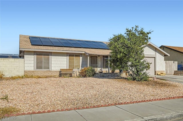 single story home featuring entry steps, a garage, solar panels, a shingled roof, and concrete driveway