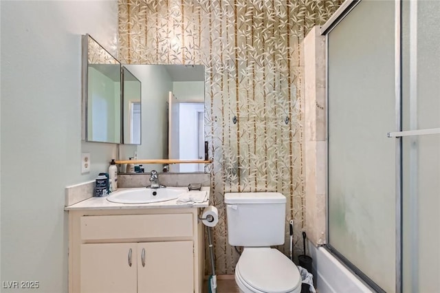 full bathroom with toilet, wallpapered walls, shower / bath combination with glass door, and vanity