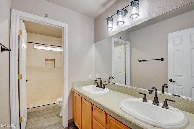 bathroom with tiled shower, a sink, toilet, and double vanity