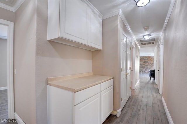 hall featuring light wood-type flooring, visible vents, ornamental molding, and baseboards