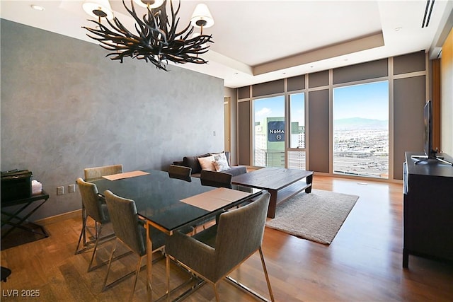 dining room featuring a notable chandelier, wood finished floors, a raised ceiling, and floor to ceiling windows