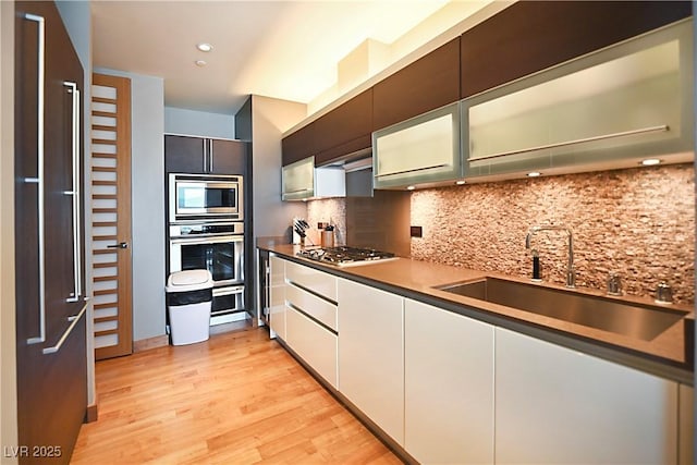 kitchen with tasteful backsplash, stainless steel appliances, light wood-style floors, white cabinetry, and a sink