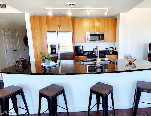 kitchen featuring appliances with stainless steel finishes, a kitchen bar, a sink, and visible vents