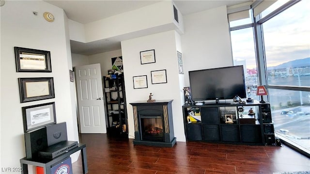 living room featuring a glass covered fireplace, floor to ceiling windows, visible vents, and wood finished floors