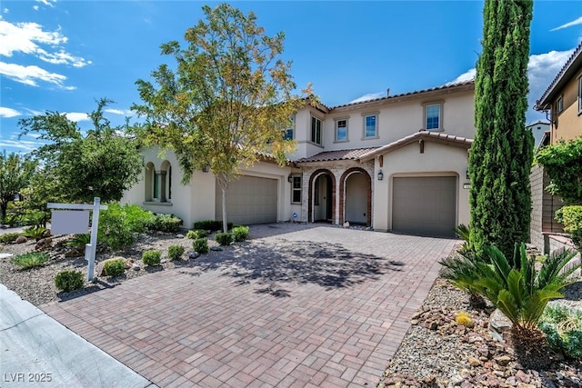 mediterranean / spanish-style house featuring a tiled roof, decorative driveway, and stucco siding