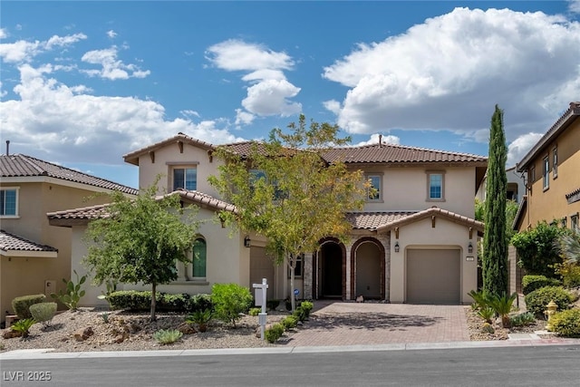 mediterranean / spanish home featuring a tiled roof, decorative driveway, and stucco siding