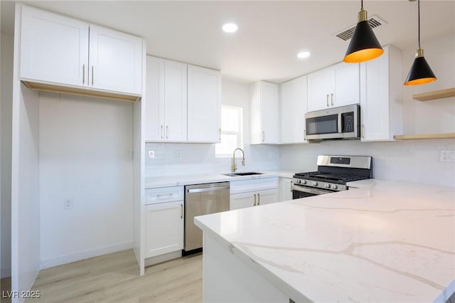 kitchen with light stone counters, appliances with stainless steel finishes, a peninsula, open shelves, and a sink