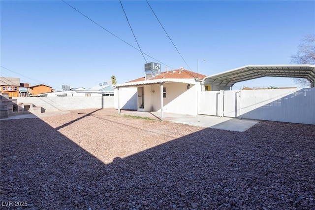 back of house featuring a detached carport, a gate, central AC, stucco siding, and fence private yard