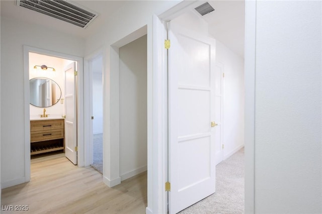 corridor with baseboards, visible vents, and light wood-type flooring