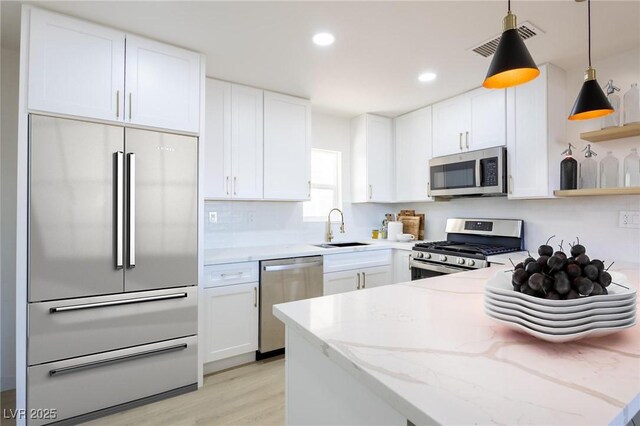 kitchen featuring a sink, light stone counters, stainless steel appliances, a peninsula, and white cabinets