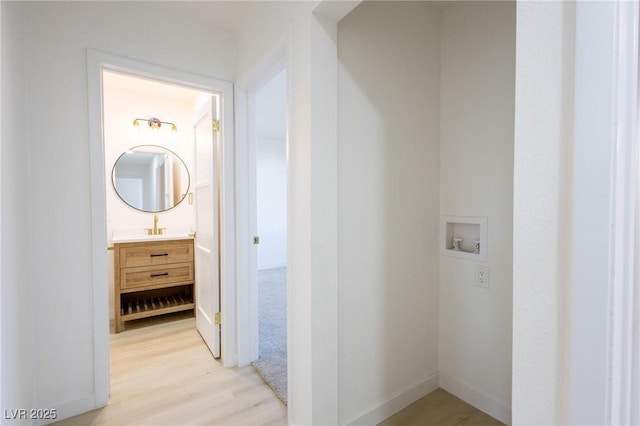 hall featuring baseboards, light wood-type flooring, and a sink