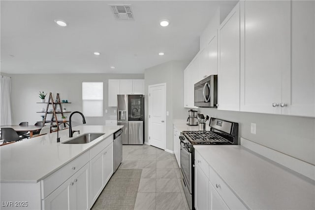 kitchen featuring visible vents, a kitchen island with sink, a sink, stainless steel appliances, and light countertops