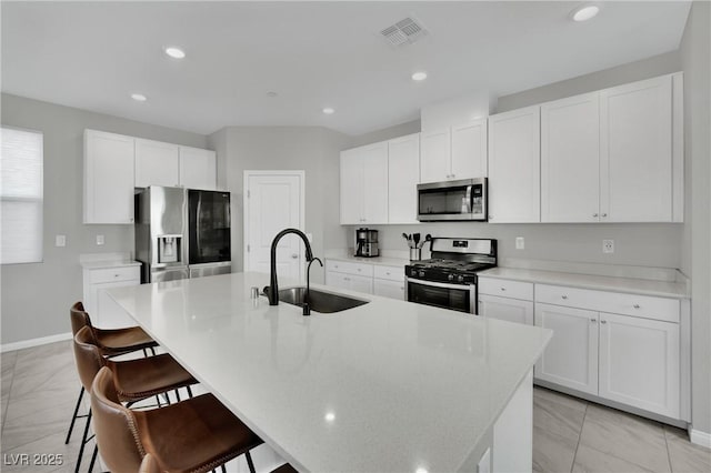 kitchen featuring visible vents, a breakfast bar, a kitchen island with sink, a sink, and appliances with stainless steel finishes