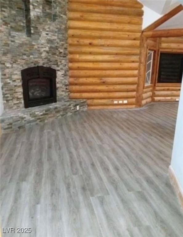 unfurnished living room featuring a stone fireplace, wood finished floors, and log walls