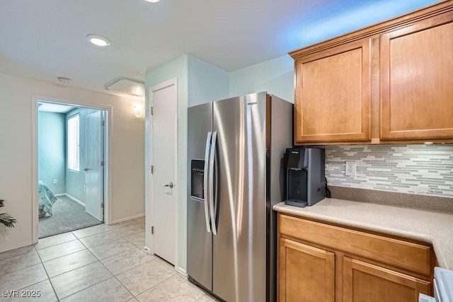 kitchen with light countertops, backsplash, brown cabinetry, light tile patterned flooring, and stainless steel fridge with ice dispenser