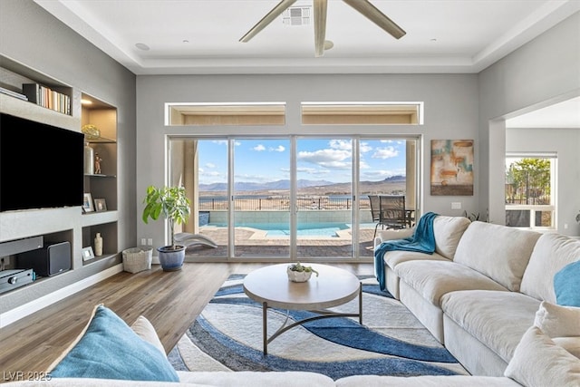 living room with built in features, a ceiling fan, visible vents, and wood finished floors