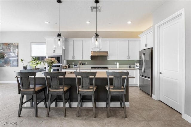 kitchen featuring a kitchen island with sink, white cabinets, light countertops, appliances with stainless steel finishes, and pendant lighting