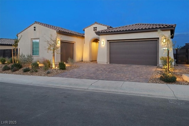 mediterranean / spanish house with a garage, decorative driveway, a tile roof, and stucco siding