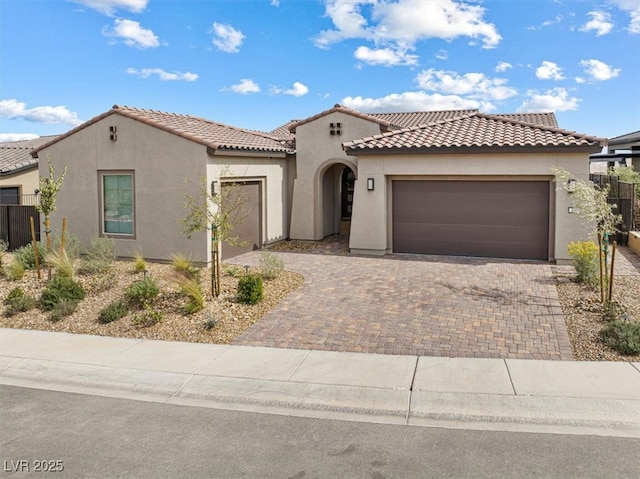 mediterranean / spanish-style house with an attached garage, a tiled roof, decorative driveway, and stucco siding