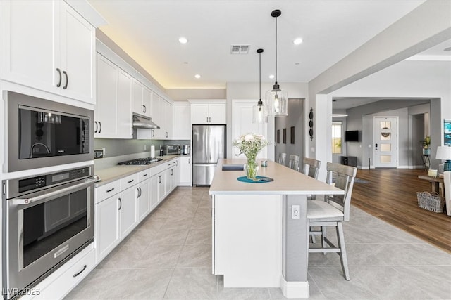 kitchen featuring a center island, stainless steel appliances, visible vents, under cabinet range hood, and a kitchen bar