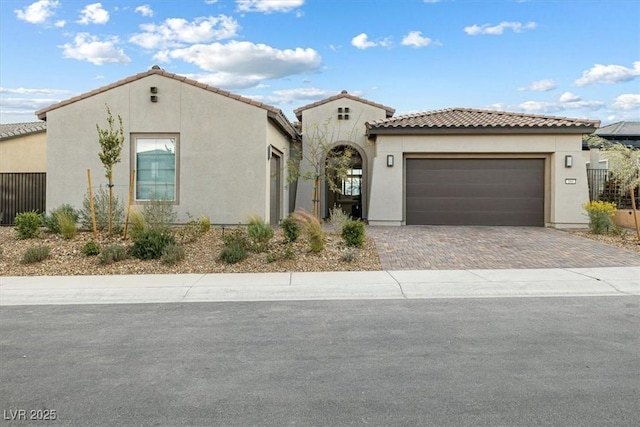 mediterranean / spanish-style house featuring a tile roof, an attached garage, fence, decorative driveway, and stucco siding