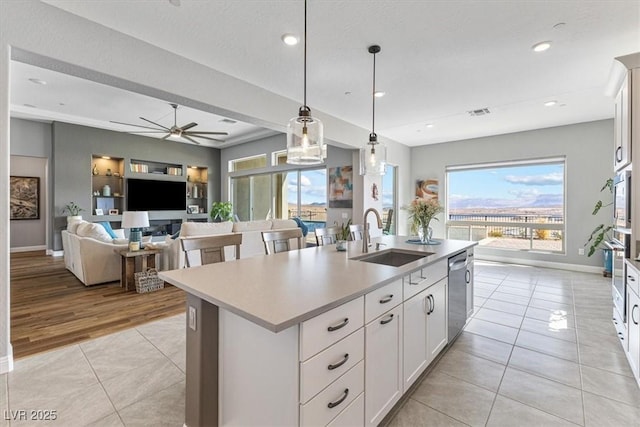 kitchen featuring a center island with sink, light tile patterned floors, light countertops, a sink, and dishwasher