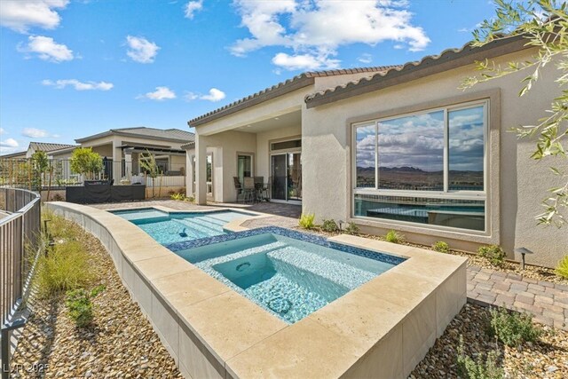 pool with an in ground hot tub, a patio area, and fence