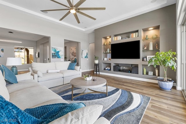 living area with baseboards, built in shelves, a tray ceiling, and wood finished floors