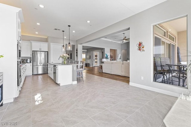 kitchen with a breakfast bar area, white cabinetry, open floor plan, stainless steel fridge, and pendant lighting