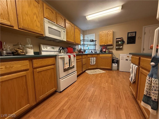 kitchen with brown cabinetry, dark countertops, white appliances, and light wood finished floors