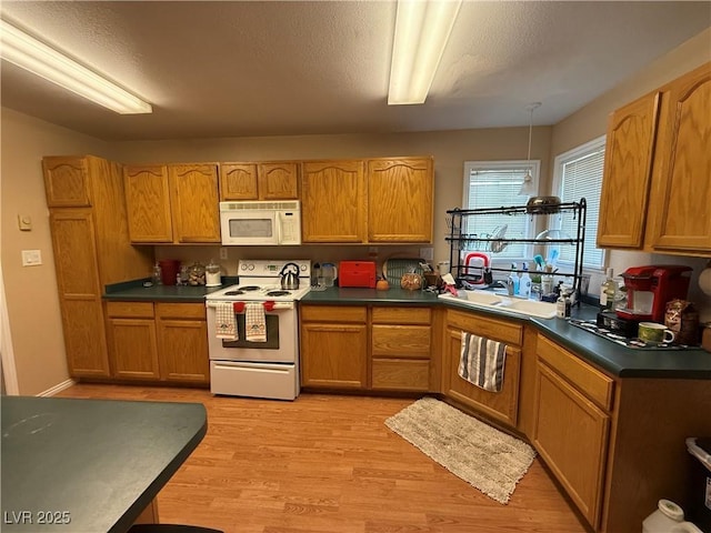 kitchen with dark countertops, white appliances, light wood-style floors, and a sink