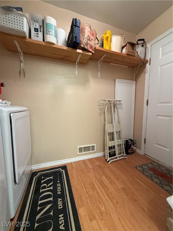 clothes washing area with laundry area, wood finished floors, visible vents, baseboards, and washing machine and clothes dryer