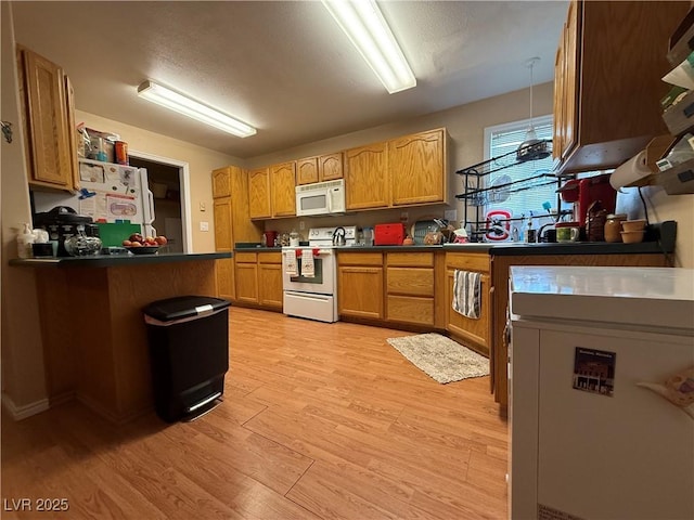 kitchen with white appliances, dark countertops, and light wood-style floors