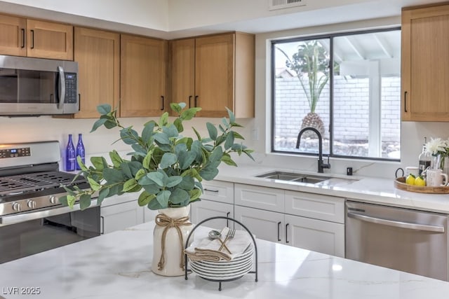 kitchen with a sink, visible vents, appliances with stainless steel finishes, brown cabinets, and light stone countertops