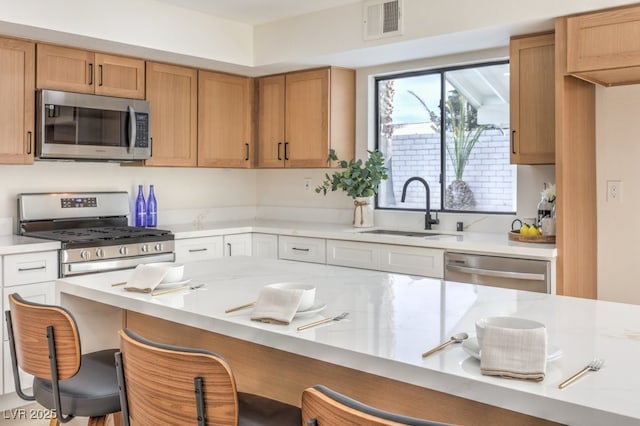 kitchen featuring a kitchen bar, visible vents, appliances with stainless steel finishes, and a sink