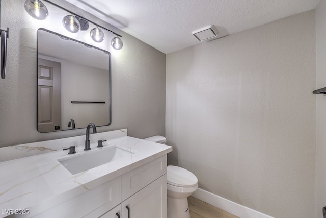 bathroom with toilet, vanity, a textured ceiling, wood finished floors, and baseboards