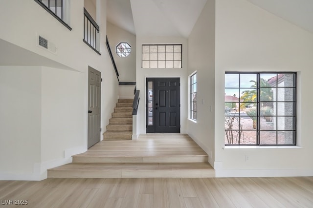 foyer featuring stairs, high vaulted ceiling, wood finished floors, and visible vents