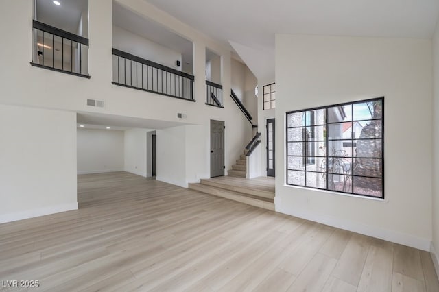 unfurnished living room featuring baseboards, visible vents, wood finished floors, a high ceiling, and stairs