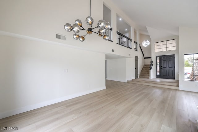 unfurnished living room featuring high vaulted ceiling, light wood-style flooring, a notable chandelier, visible vents, and stairway